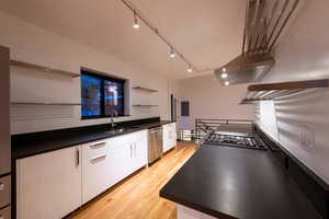 Kitchen with open shelves,  quartz leather-top black counter tops light wood-style flooring, white cabinets, and rail lighting, gas range