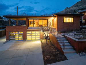 View of front of home with concrete driveway, an attached garage, custom LED lighting, attractive rusted steel walls, outdoor lighting.