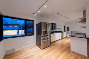 Kitchen featuring GE PROFILE stainless steel appliances, light wood-style flooring, open shelves, track lighting, and exhaust hood