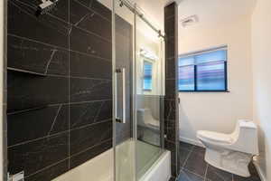 Full bathroom with toilet and shower / bath combination with glass door, imported tile