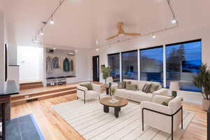 Living room with track lighting, ceiling fan, and light wood finished floors