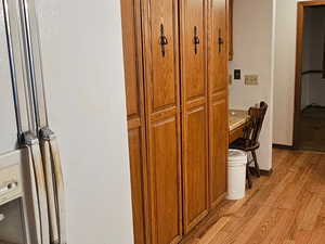 Kitchen featuring crown molding, wood finish cabinets, white refrigerator with ice dispenser, light wood-style floors, and light countertops