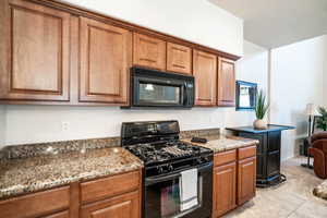 Kitchen featuring black appliances, wood finish cabinetry, dark stone countertops, and light tile patterned flooring