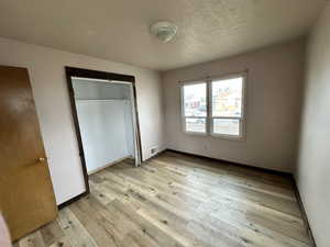 Unfurnished bedroom with light wood-type flooring, a closet, and a textured ceiling