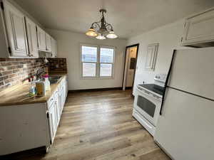 Kitchen with white cabinets, white appliances, a chandelier, light wood finished floors, and decorative backsplash