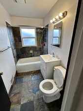 Full bathroom featuring vanity, bathtub / shower combination, dark stone finish floors, and a textured wall