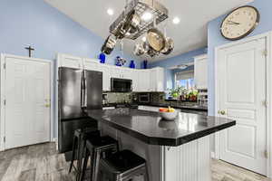 Kitchen with stainless steel appliances, white cabinets, a kitchen bar, vaulted ceiling, and decorative backsplash