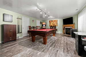 Playroom featuring pool table, a tile fireplace, a textured ceiling, wood finished floors, and rail lighting
