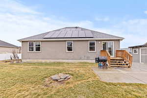 Back of property with roof mounted solar panels, a shingled roof, and stucco siding