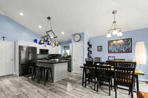 Kitchen with hanging lights, vaulted ceiling, freestanding refrigerator, a kitchen bar, and a kitchen island