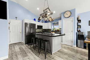Kitchen with a breakfast bar, freestanding refrigerator, a kitchen island, white cabinets, and vaulted ceiling