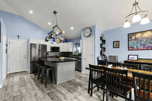 Kitchen featuring a kitchen breakfast bar, stainless steel appliances, a kitchen island, lofted ceiling, and a chandelier