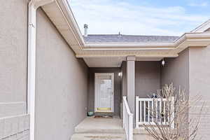 View of exterior entry featuring stucco siding and roof with shingles