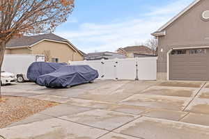 View of side of property with a gate, concrete driveway, stucco siding, and a garage