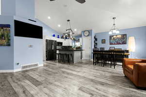 Living room featuring suspended lighting, lofted ceiling, light wood-style floors, and ceiling fan