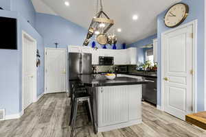 Kitchen featuring white cabinets, a kitchen breakfast bar, stainless steel appliances, tasteful backsplash, and vaulted ceiling