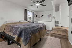 Bedroom with wood finished floors, a heating unit, a ceiling fan, a textured ceiling, and cooling unit