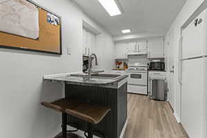 Kitchen with white cabinets, white appliances, a peninsula, dark countertops, and a breakfast bar area