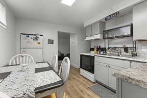 Kitchen with gray cabinets, range with electric cooktop, freestanding refrigerator, light wood finished floors, and decorative backsplash