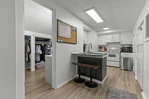 Kitchen featuring a peninsula, white cabinets, a breakfast bar area, white appliances, and light wood finished floors