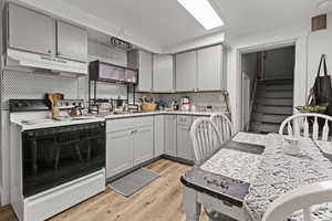 Kitchen featuring gray cabinetry, range with electric cooktop, light wood-style flooring, tasteful backsplash, and extractor fan