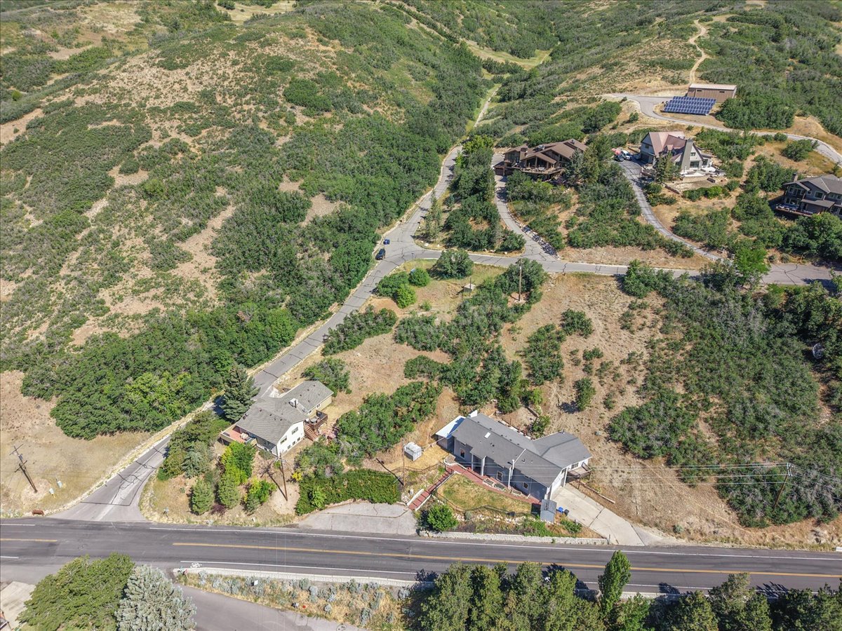 Expansive hillside property featuring a multi-level residence with a gray exterior, surrounding natural landscape, and paved road frontage