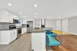 Kitchen with stainless steel appliances, white cabinetry, a kitchen island with sink, decorative backsplash, and recessed lighting