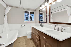 Full bathroom featuring wainscoting, a freestanding tub, double vanity, and light tile patterned floors