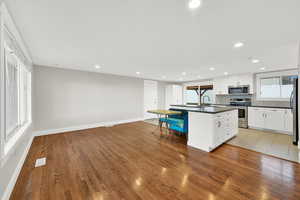 Kitchen with an island with sink, stainless steel appliances, white cabinetry, light wood-style floors, and decorative backsplash