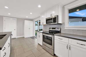 Kitchen featuring stainless steel appliances, white cabinetry, tasteful backsplash, recessed lighting, and dark stone counters