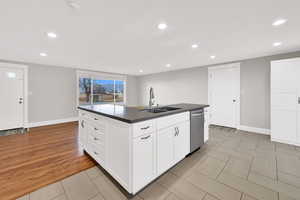Kitchen featuring dark countertops, white cabinets, recessed lighting, a center island with sink, and stainless steel dishwasher