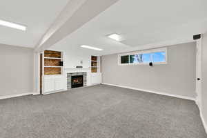 Below grade area featuring built in features, light carpet, and a tiled fireplace