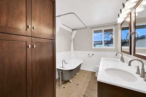 Full bath featuring wainscoting, a soaking tub, double vanity, and light tile patterned floors