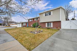 Split level home featuring a gate, brick siding, and concrete driveway