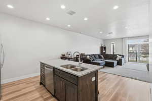 Kitchen with dark wood finish cabinetry, light stone countertops, light wood-style floors, a center island with sink, and recessed lighting