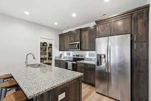 Kitchen with dark wood finish cabinets, stainless steel appliances, light stone countertops, a kitchen breakfast bar, and an island with sink