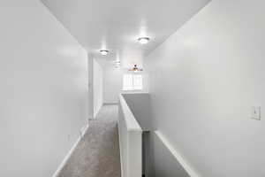 Corridor with an upstairs landing, light carpet, and a textured ceiling