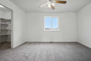 Unfurnished bedroom with a walk in closet, light carpet, and a ceiling fan