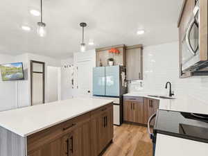 Kitchen featuring black electric range, hanging light fixtures, stainless steel microwave, light wood-type flooring, and freestanding refrigerator
