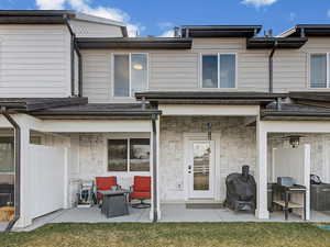 Rear view of property with a patio area, a lawn, and stone siding