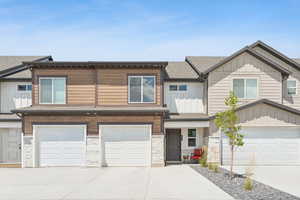 View of front facade, driveway, a garage, roof with shingles, stone siding and space to sit in the shade