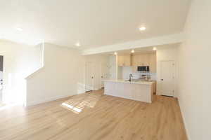 Kitchen featuring a kitchen island with sink, light countertops, open floor plan, light wood-style floors, and stainless steel appliances