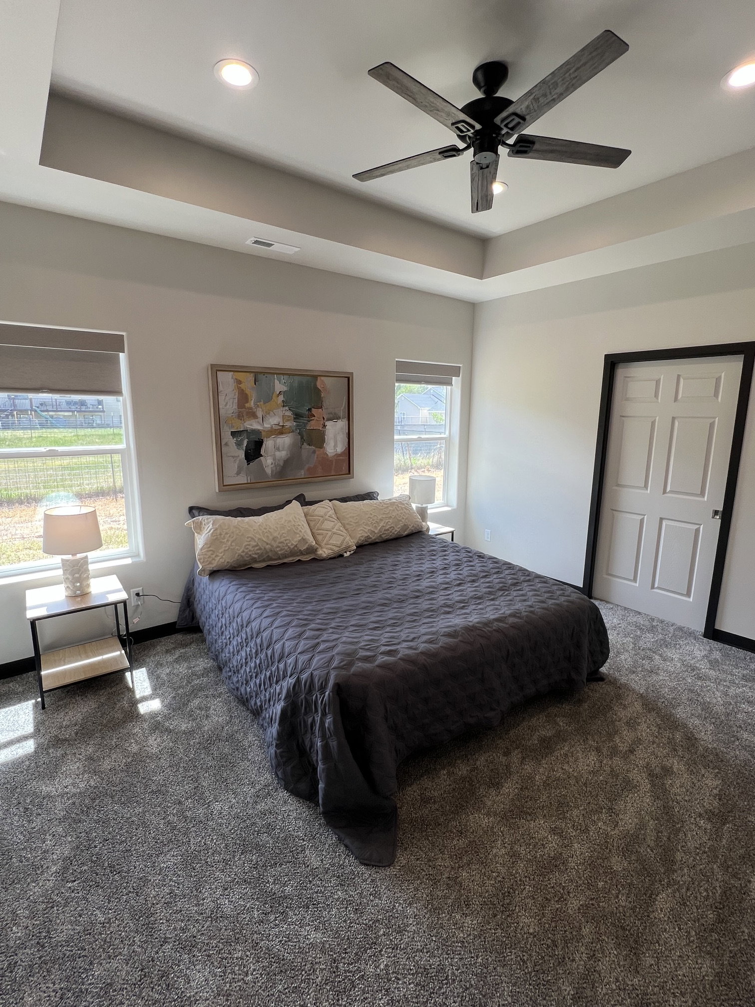 Spacious room featuring a tray ceiling with recessed lighting and a ceiling fan, two windows with blinds, and plush carpeting