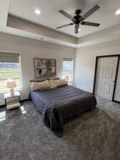 Spacious room featuring a tray ceiling with recessed lighting and a ceiling fan, two windows with blinds, and plush carpeting