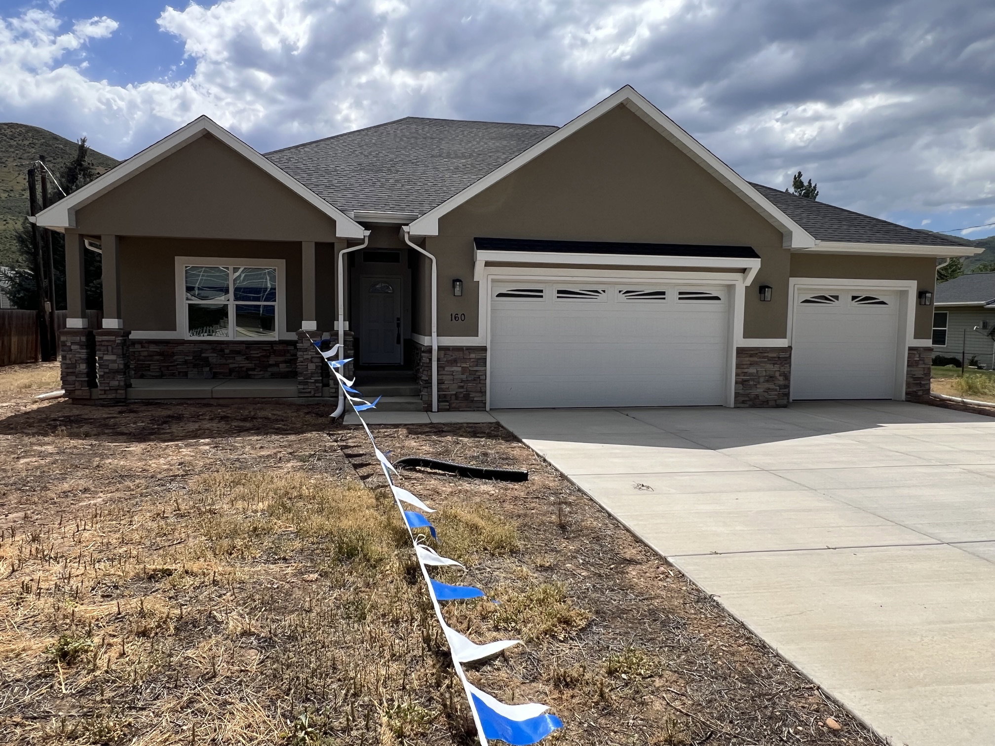 Contemporary ranch-style residence featuring a prominent two-car garage, stone veneer accents, stucco exterior finish, and a covered entryway