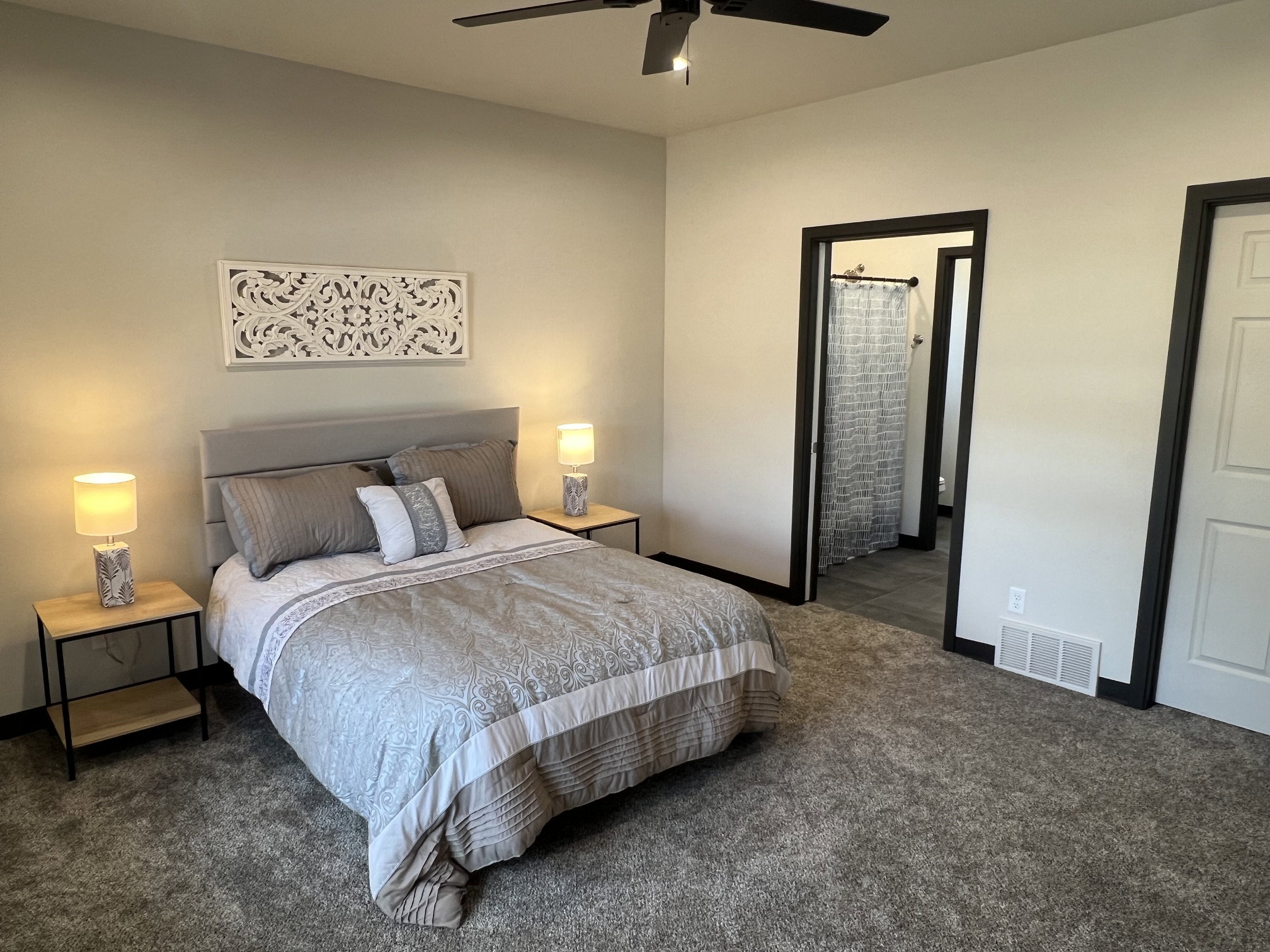 Carpeted bedroom featuring a black ceiling fan, light gray walls, an upholstered headboard, and dark trim around doorways