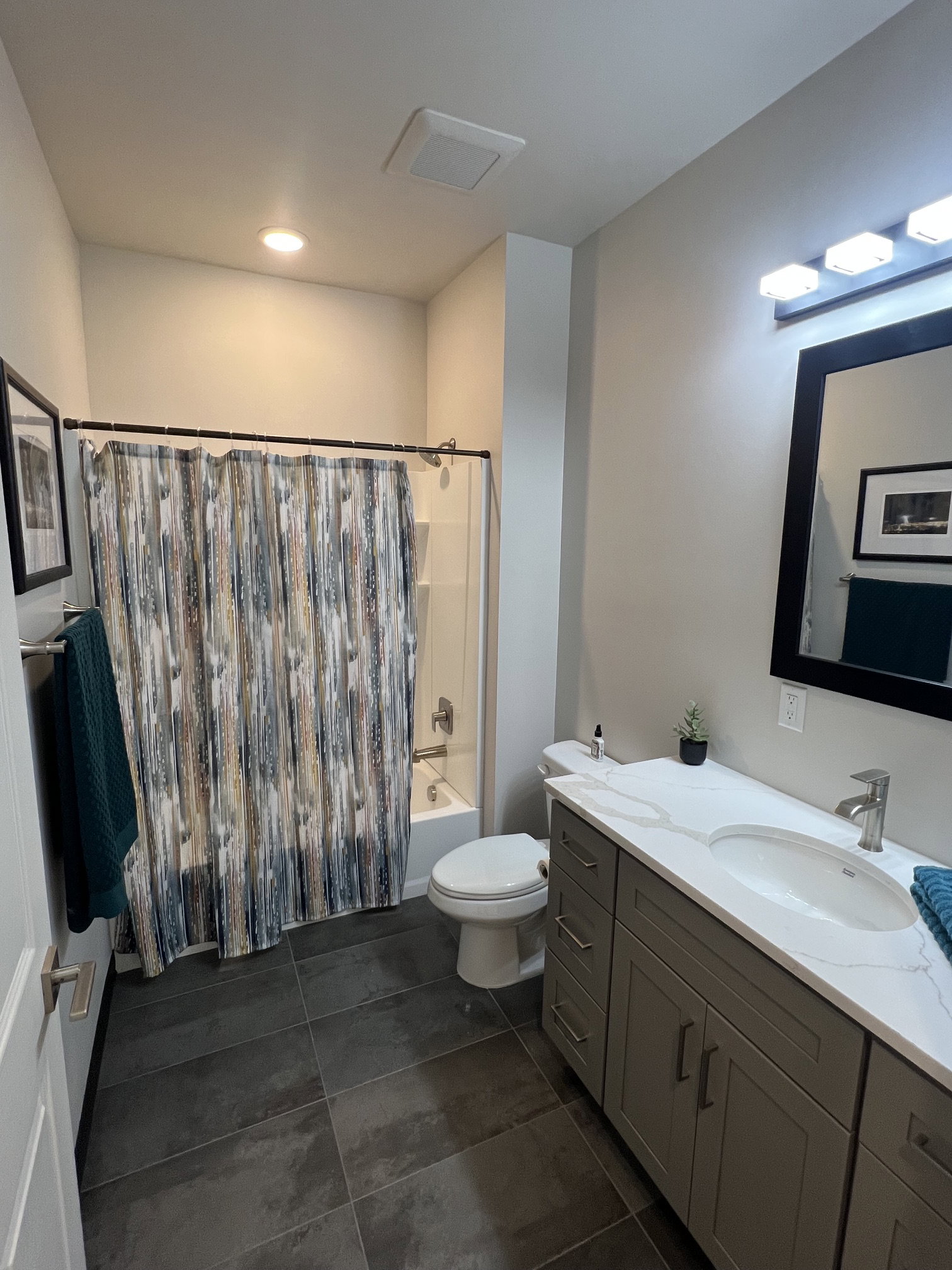 Full bathroom featuring a single shower-tub combination, a toilet, a vanity with double sinks, and dark tile flooring