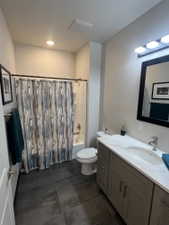 Full bathroom featuring a single shower-tub combination, a toilet, a vanity with double sinks, and dark tile flooring
