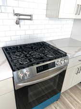 Kitchen view of stainless steel range with gas stovetop, white cabinetry, pot filler, and light stone countertops