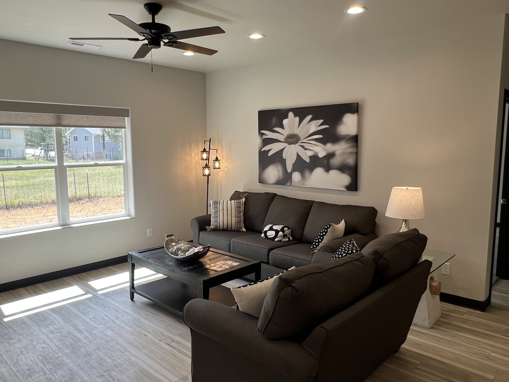 Spacious living area featuring wood-finish flooring, a large window with roller shades, a ceiling fan, and recessed lighting
